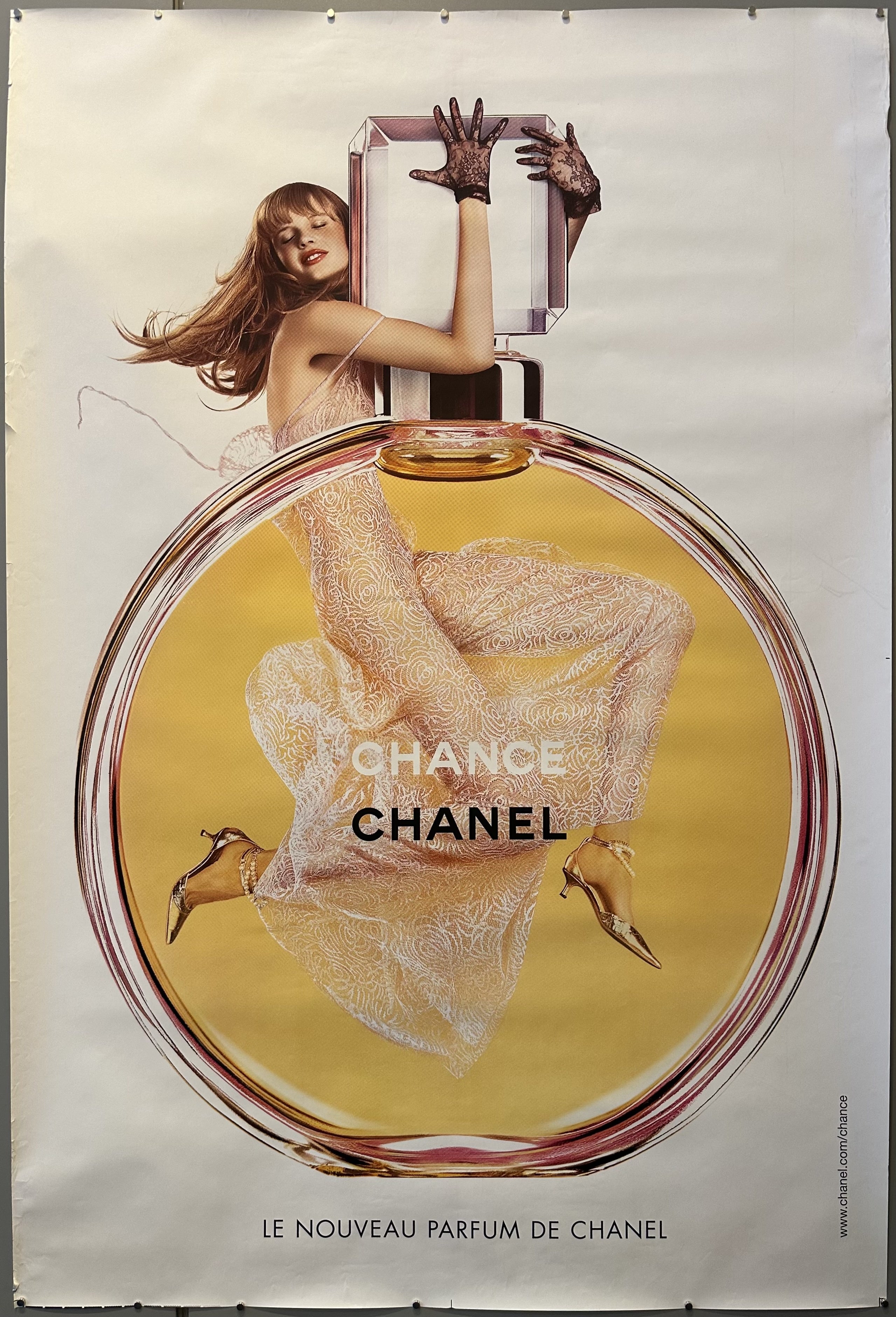Poster for Chanel 'Chance' with model holding onto perfume bottle against white background.