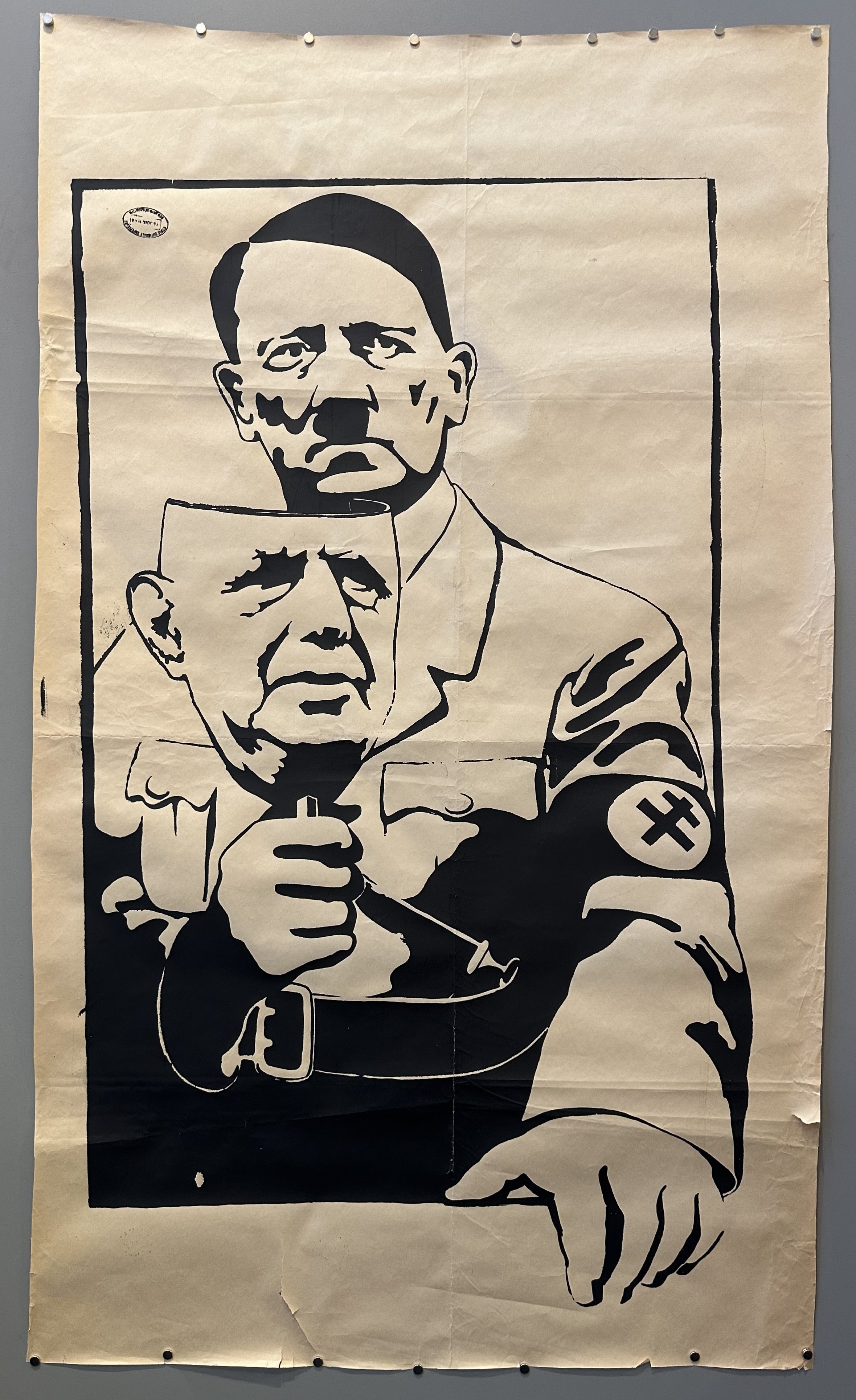 Poster showing Adolf Hitler, wearing the Cross of Lorraine instead of a swastika on his armband, and peering out from behind the mask of De Gaulle that he is holding.