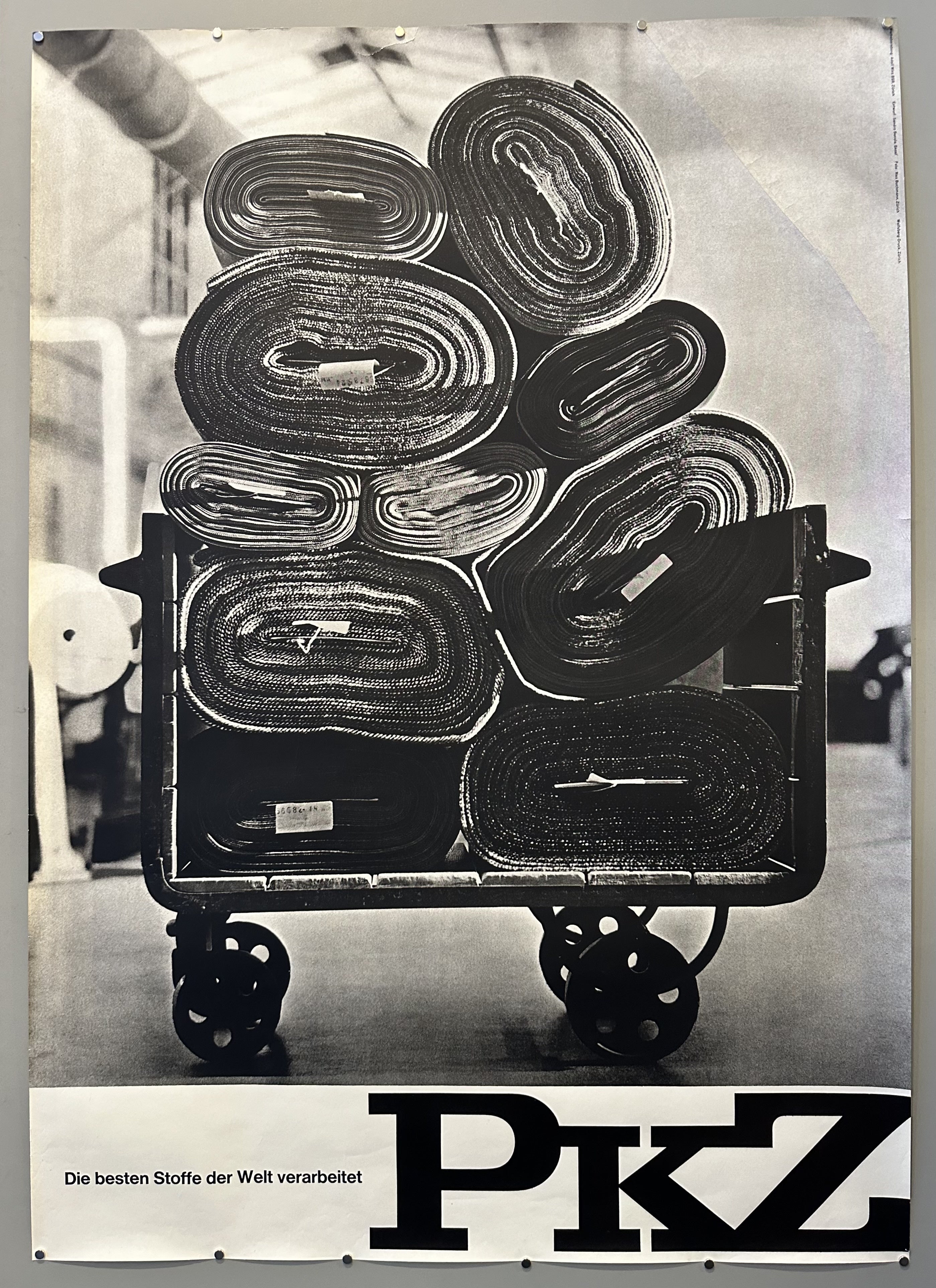 Black and white poster with rugs rolled and stacked on top of each other for PKZ department store advertisement.