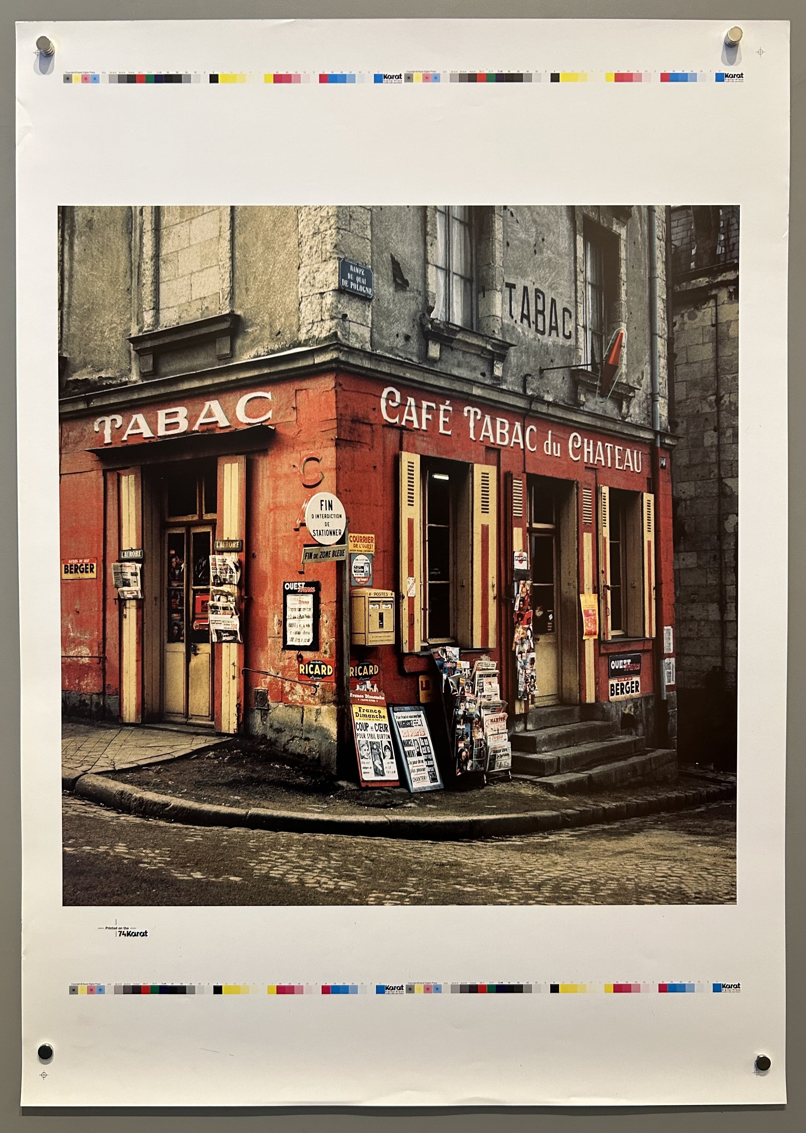 Photograph proof of French tabac with red exterior and magazine stands outside.
