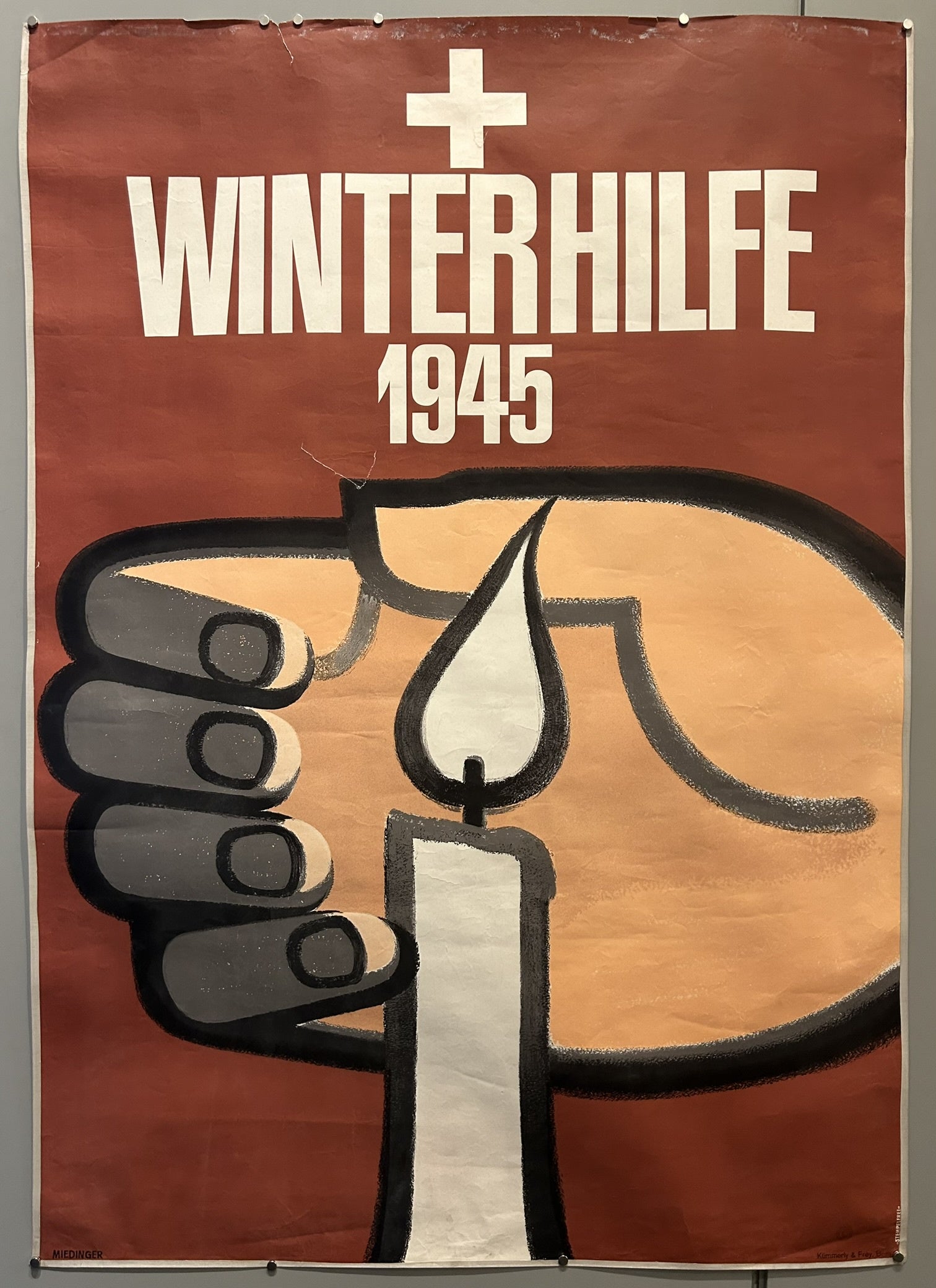 The lit candle symbolizes hope and warmth, while the hand holding it represents support and assistance provided to those in need. The cross symbol is often associated with humanitarian or religious aid organizations, such as the Swiss Winter Relief.