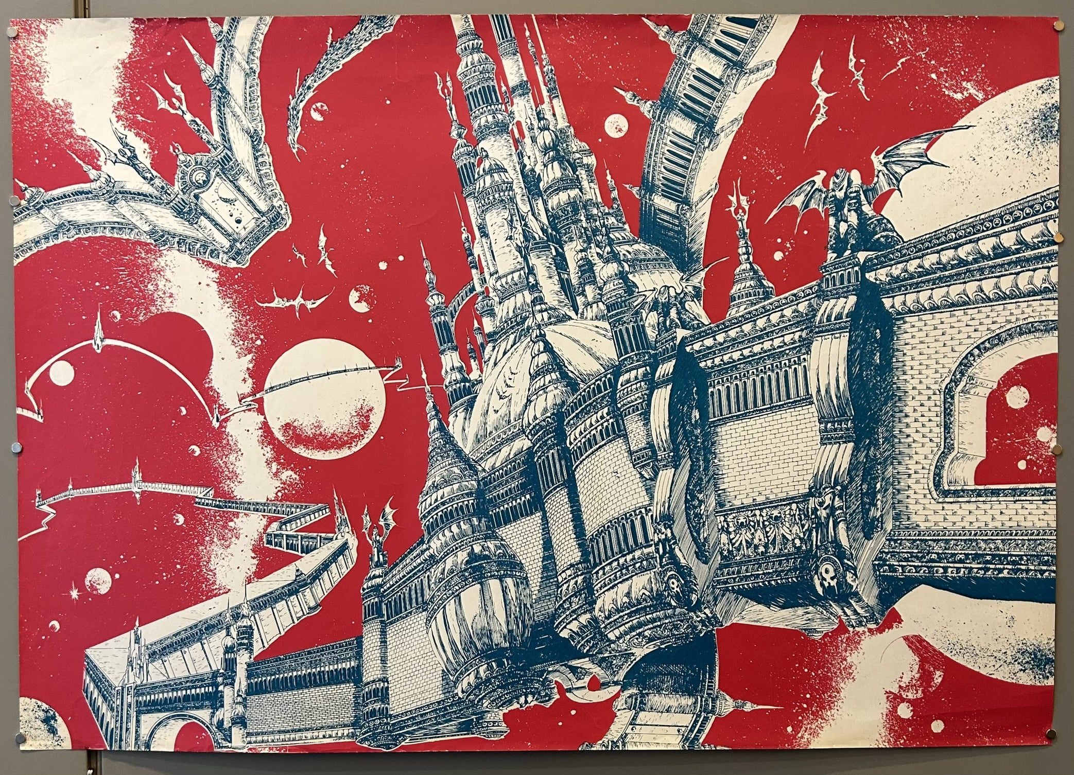 An illustration in red and white by Philippe Druillet, titled "The Mighty One," depicts a fantastical, elaborate castle-like structure with intricate architectural details, spires, and bridges, seemingly floating in a cosmic setting with celestial bodies and flying creatures resembling dragons or gargoyles.