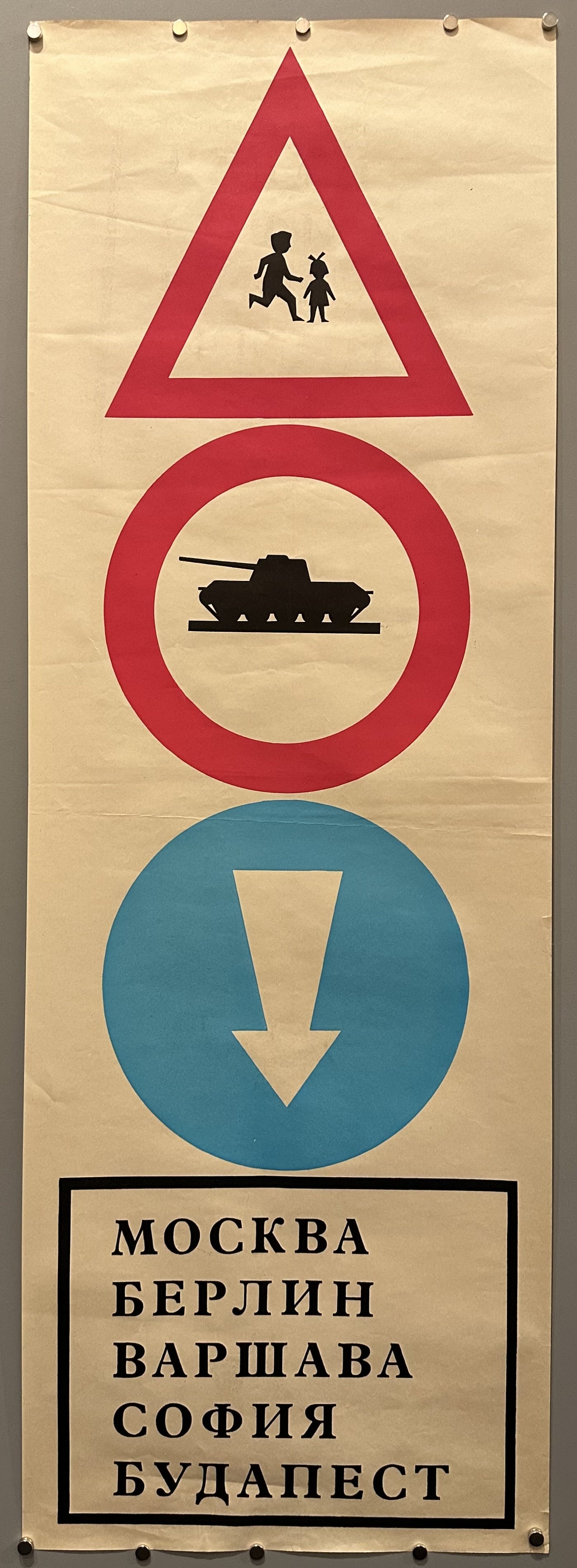 Image of three road traffic signs: children running, tanks driving and an arrow pointing to a list that reads Moscow, Berlin, Warsaw, Sofia, Budapes