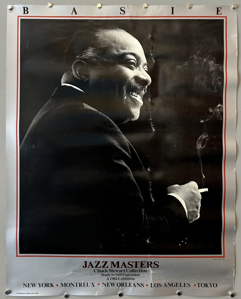 A black and white poster featuring a smiling Count Basie, holding a cigarette with smoke rising. The top of the poster has the letters "B A S I E" spelled out with pins