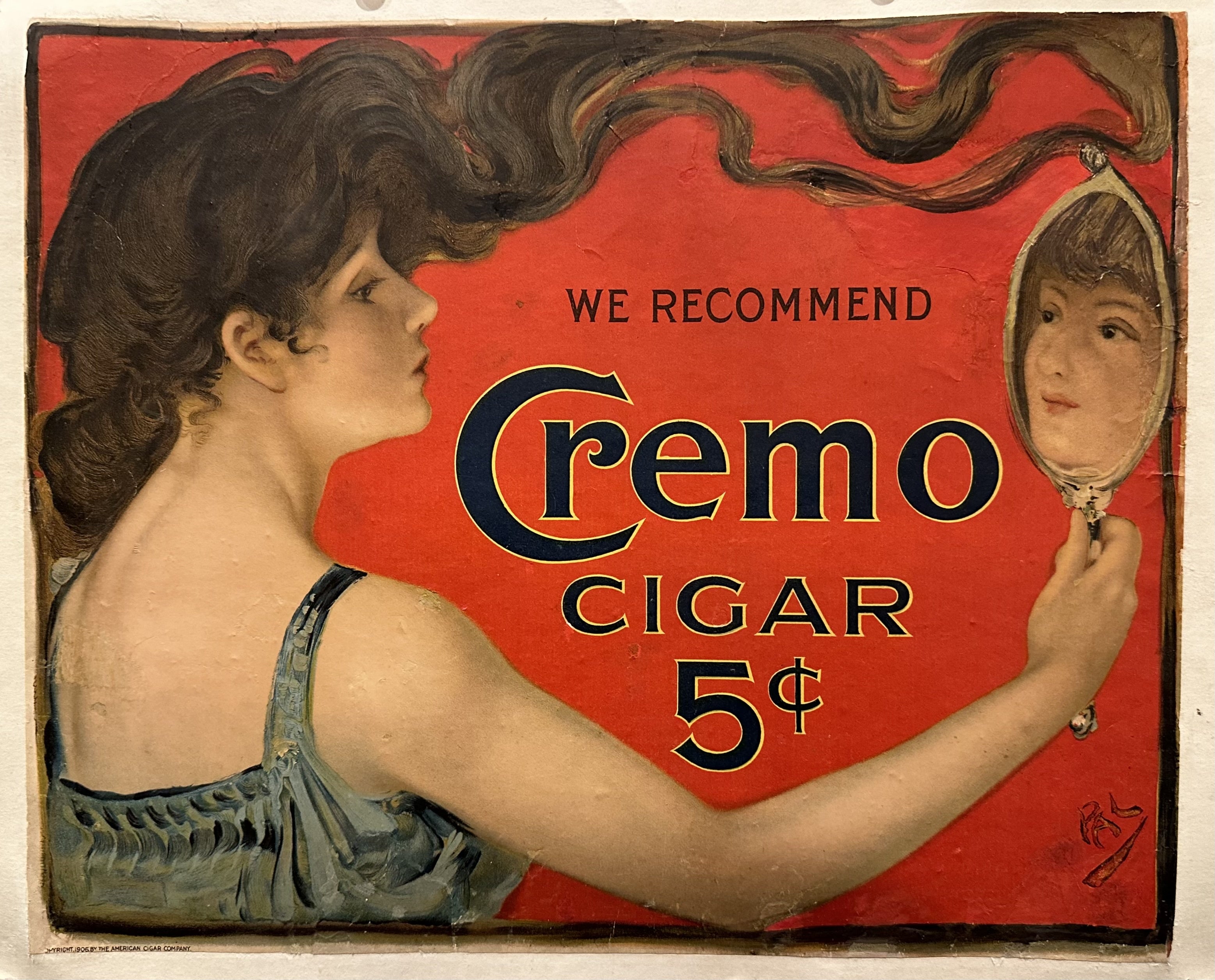 Small red vintage cigar advertisement with a woman looking at herself in a handheld mirror.