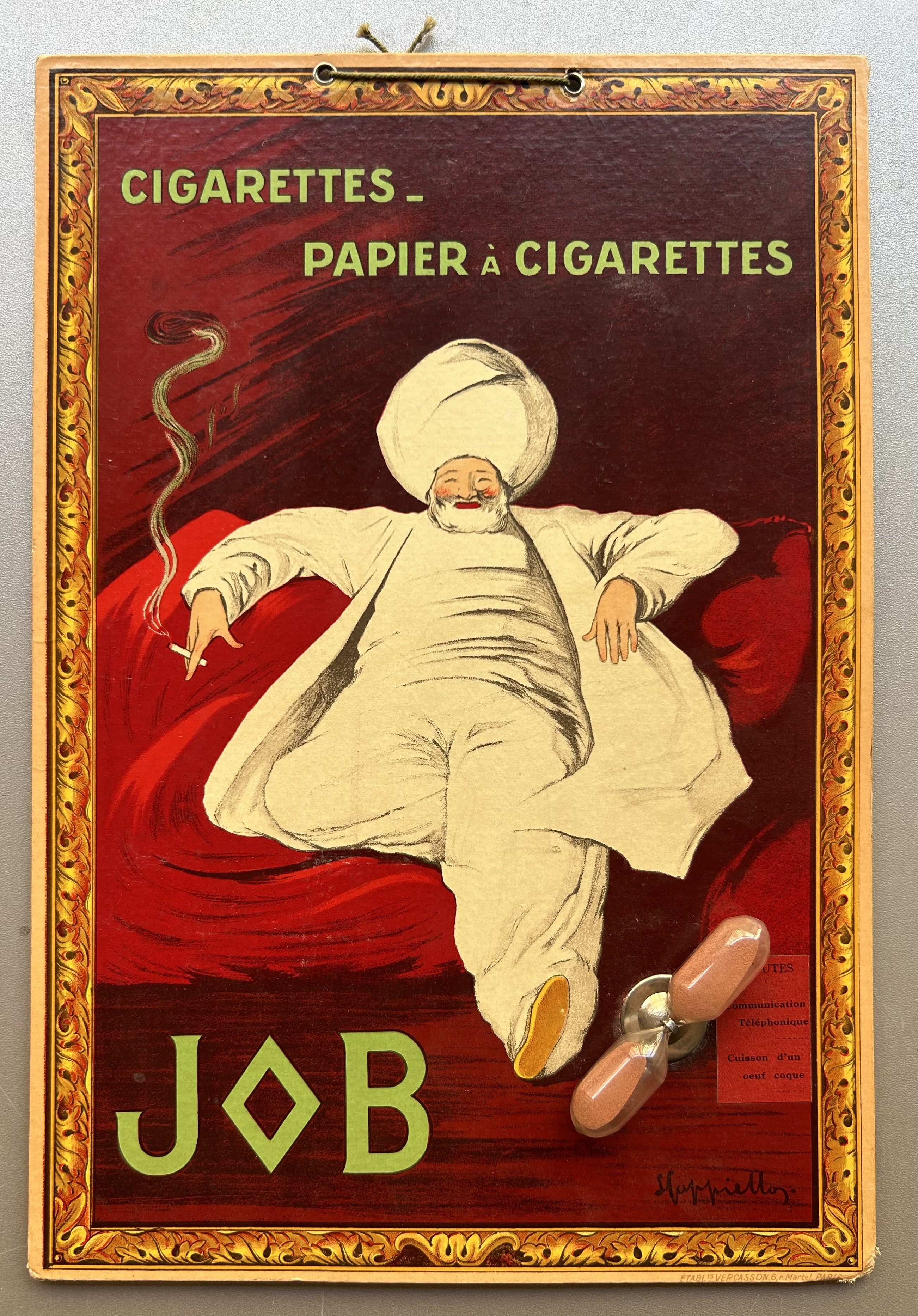 Hourglass sand timer is attached with metal spinning bracket on bottom right-hand corner, with illustration of sultan smoking a cigarette lounging on red pillows.