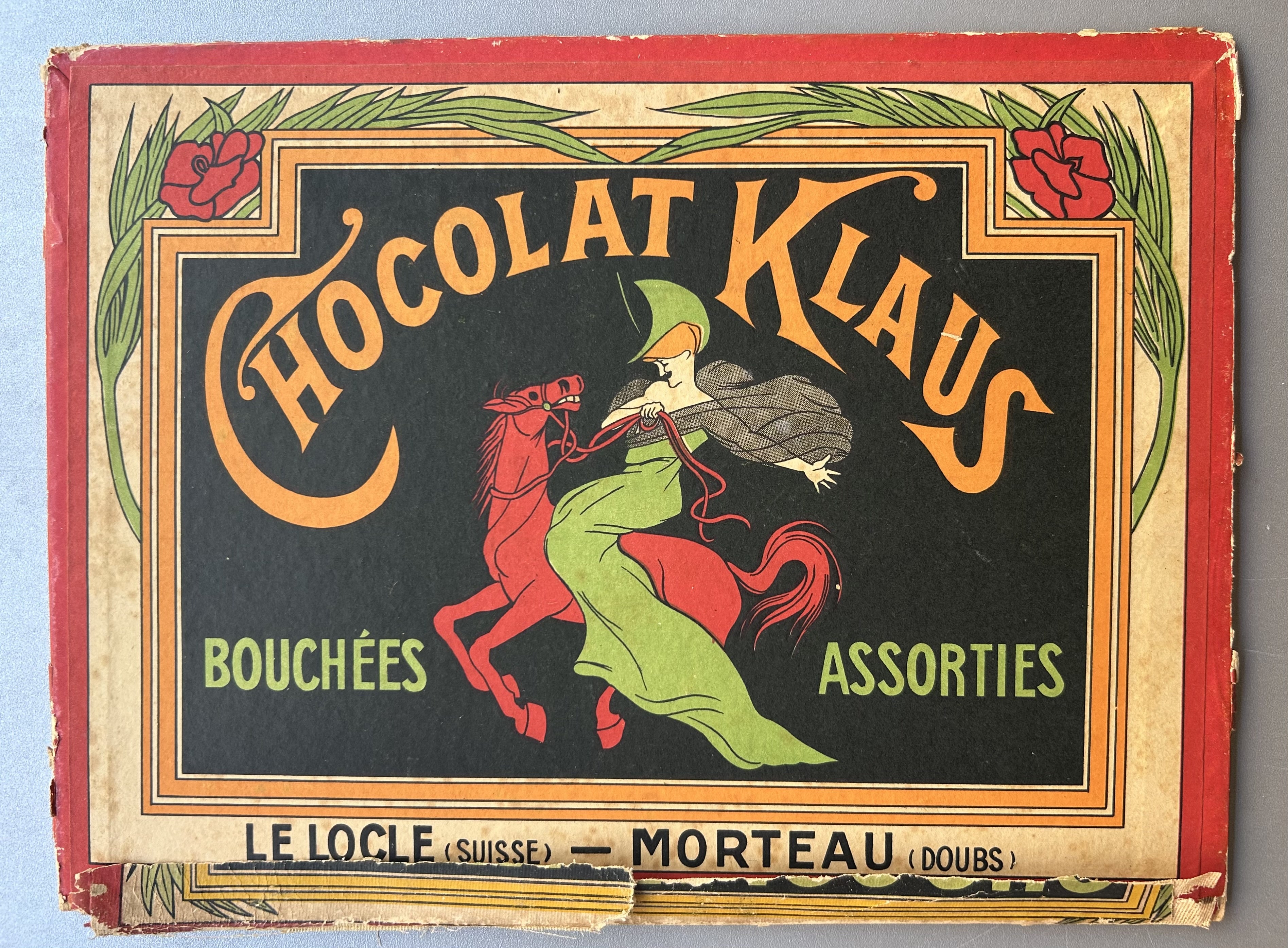 Cardboard chocolate box for Chocolat Klaus, written in orange text with floral border and green accent text below.