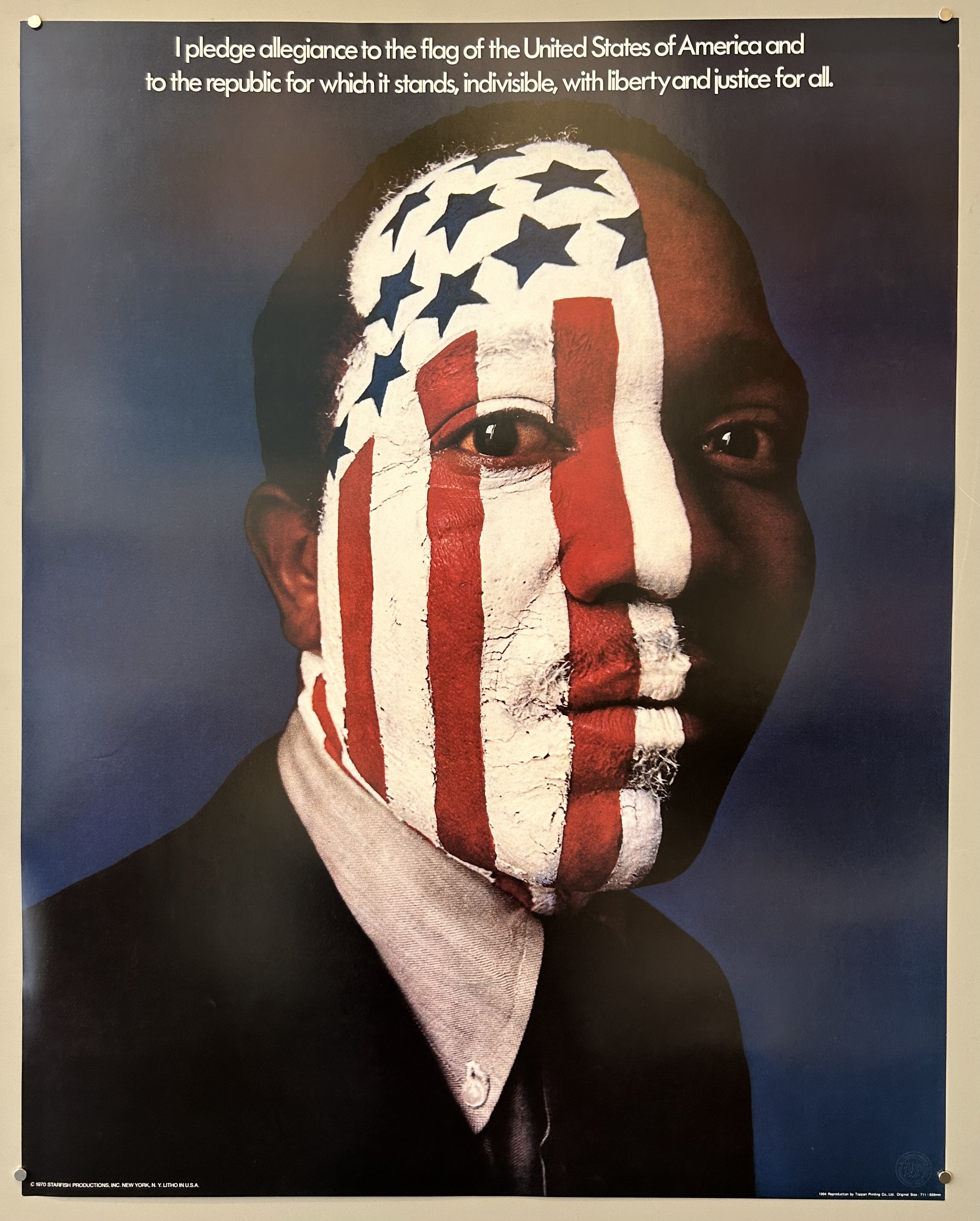 Photograph of a male portrait with the American flag painted on his face and white typography above against a blue background.