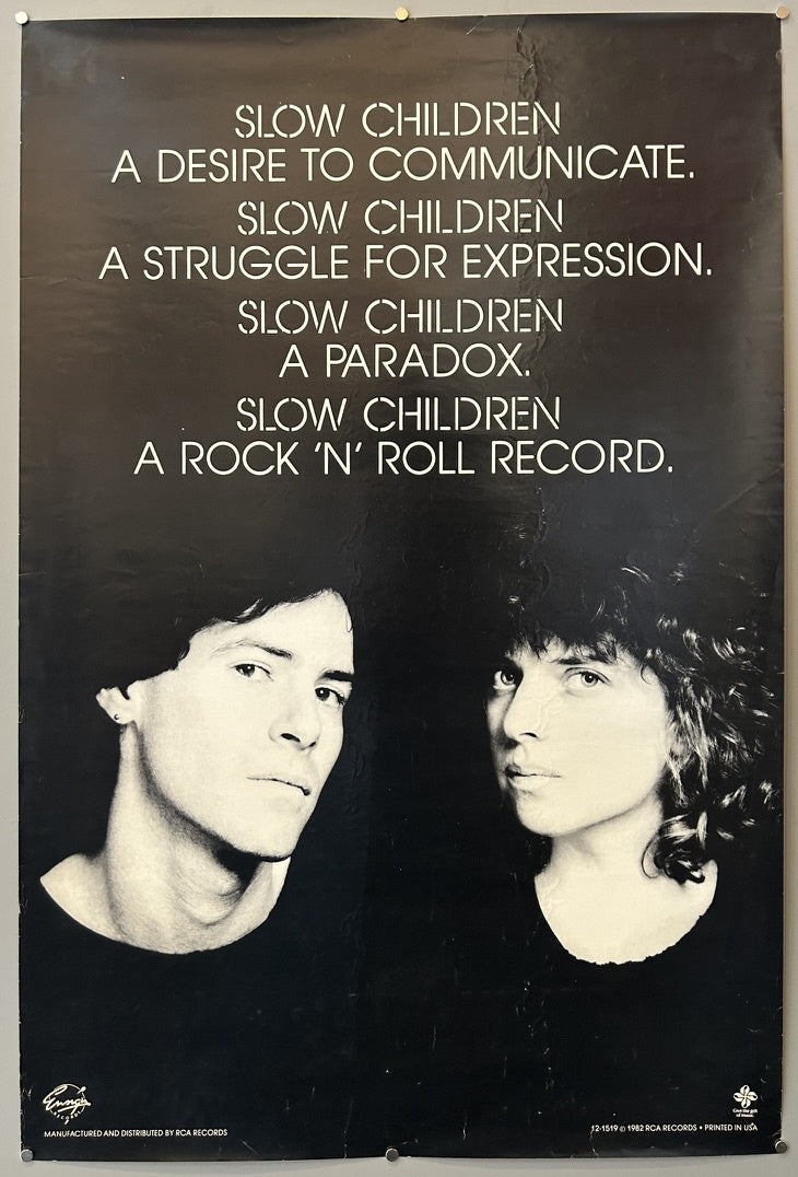A black and white poster featuring two individuals, one on the left with shorter, dark hair and one on the right with curly, dark hair. Above them, white text reads:
"SLOW CHILDREN
A DESIRE TO COMMUNICATE.
SLOW CHILDREN
A STRUGGLE FOR EXPRESSION.
SLOW CHILDREN
A PARADOX.
SLOW CHILDREN
A ROCK 'N' ROLL RECORD."