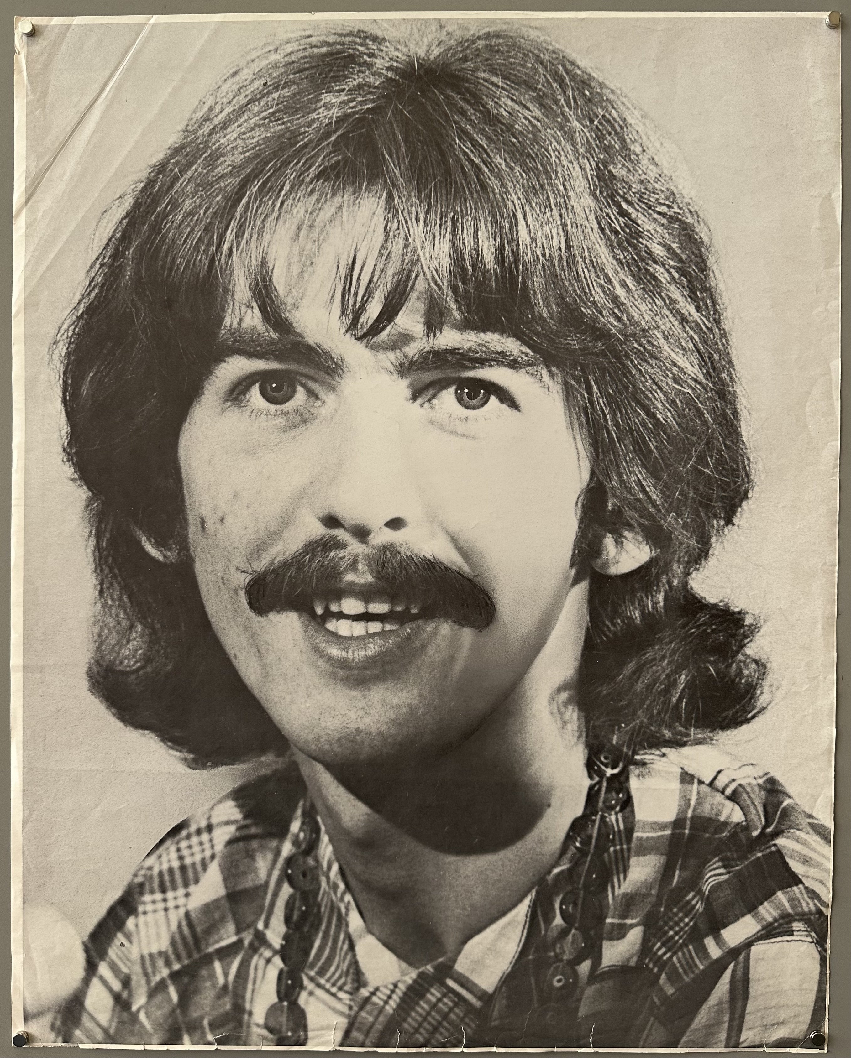 Black and white photograph portrait of George Harrison of the Beatles, looking direclty at the camera, smiling.