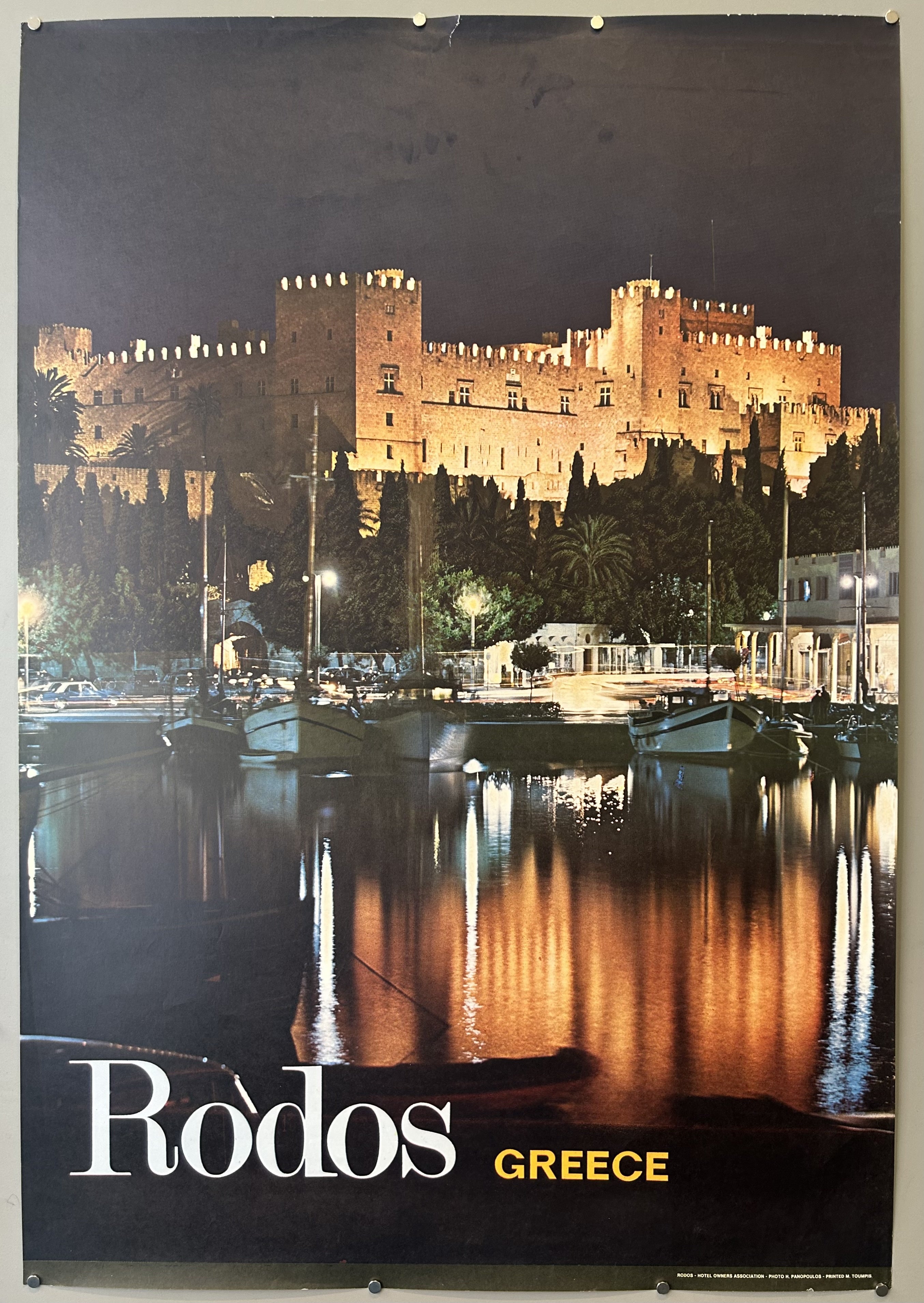 Photograph of the Kastello at night in vintage travel poster from Rhodes Hotel Association, 'Rodos' written along bottom left-hand side.