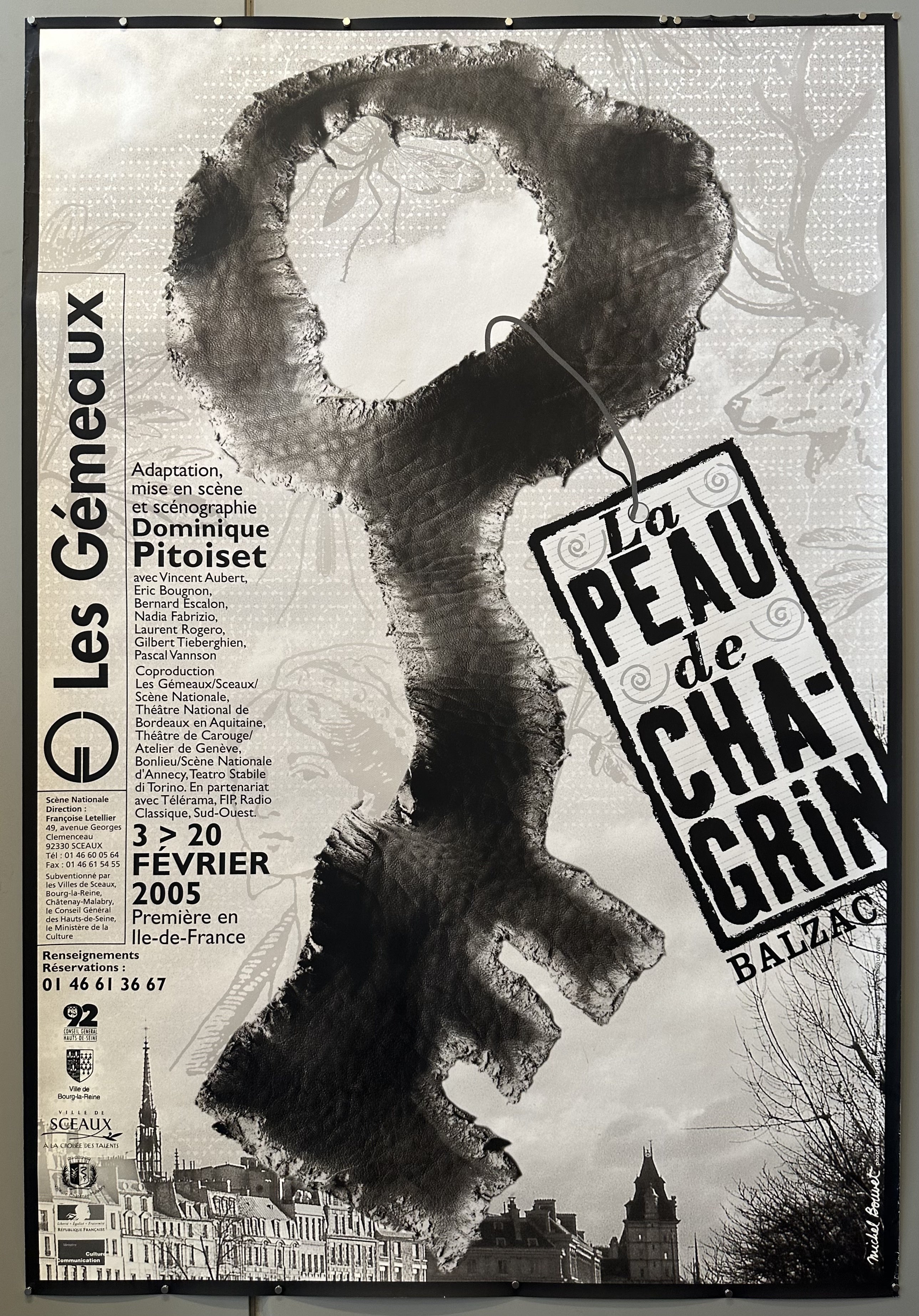 Black and white poster with a key overlaid on a photograph of a village to promote a show at the Les Gemeaux in France.