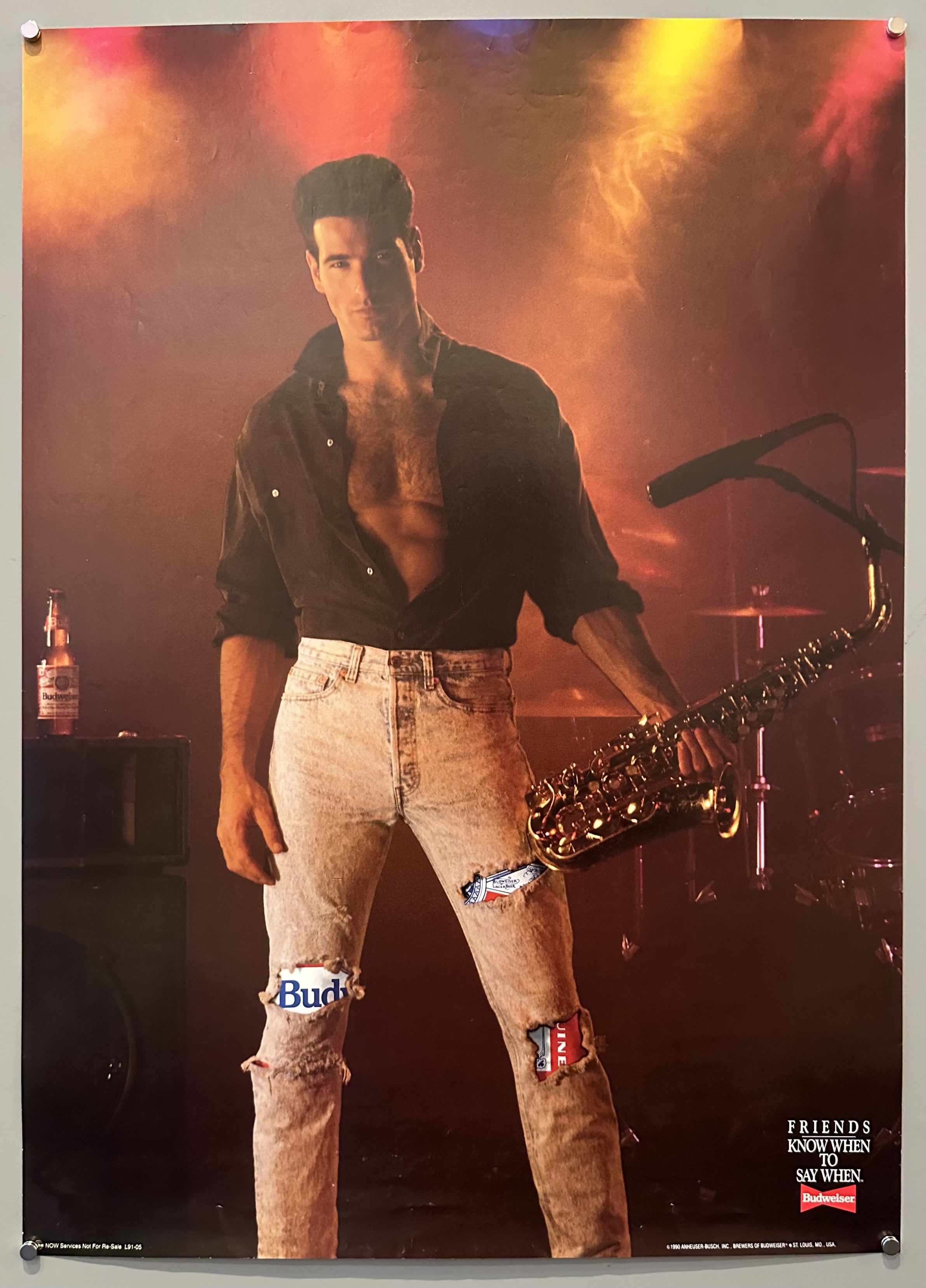 A man holds a tuba with ripped jeans on and a Budweiser next to him in advertisement.