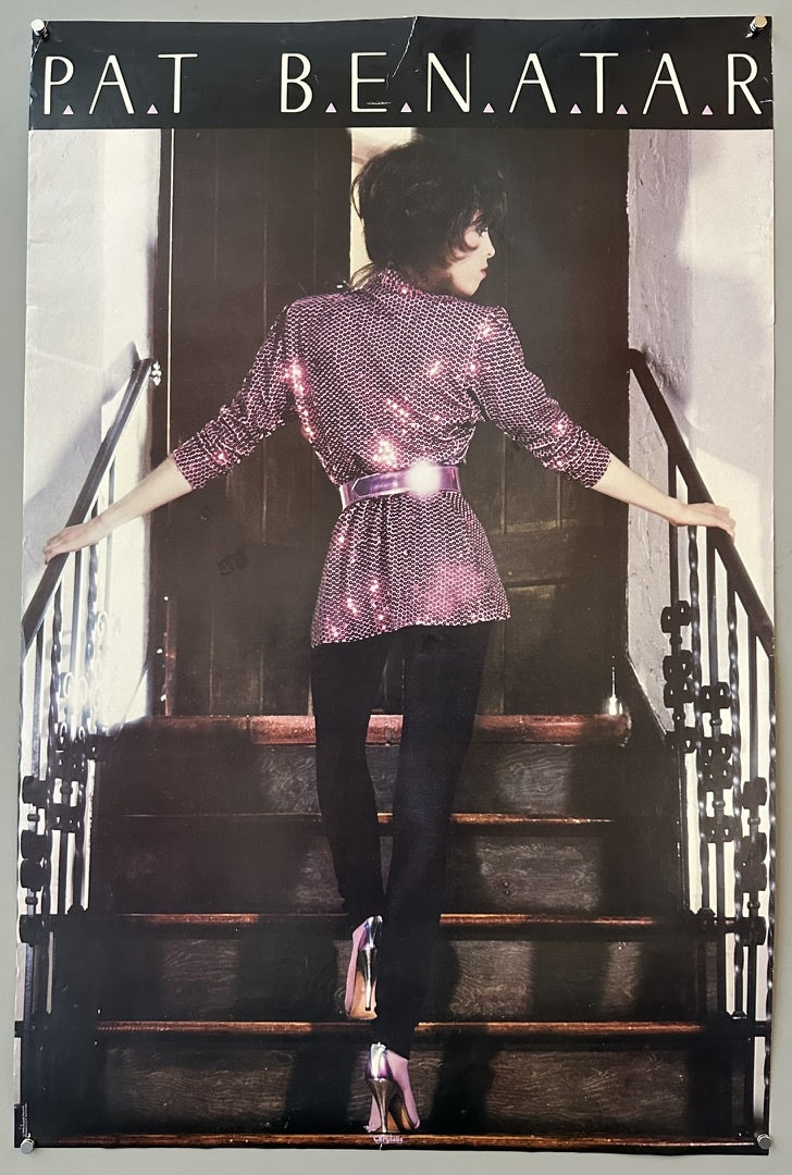 A full-length poster of Pat Benatar, seen from behind, walking up a set of stairs. She is wearing a sparkling pink long-sleeved top with a wide purple belt, black pants, and silver high heels. Her hair is short and dark. The text "P.A.T B.E.N.A.T.A.R" is at the top of the poster.