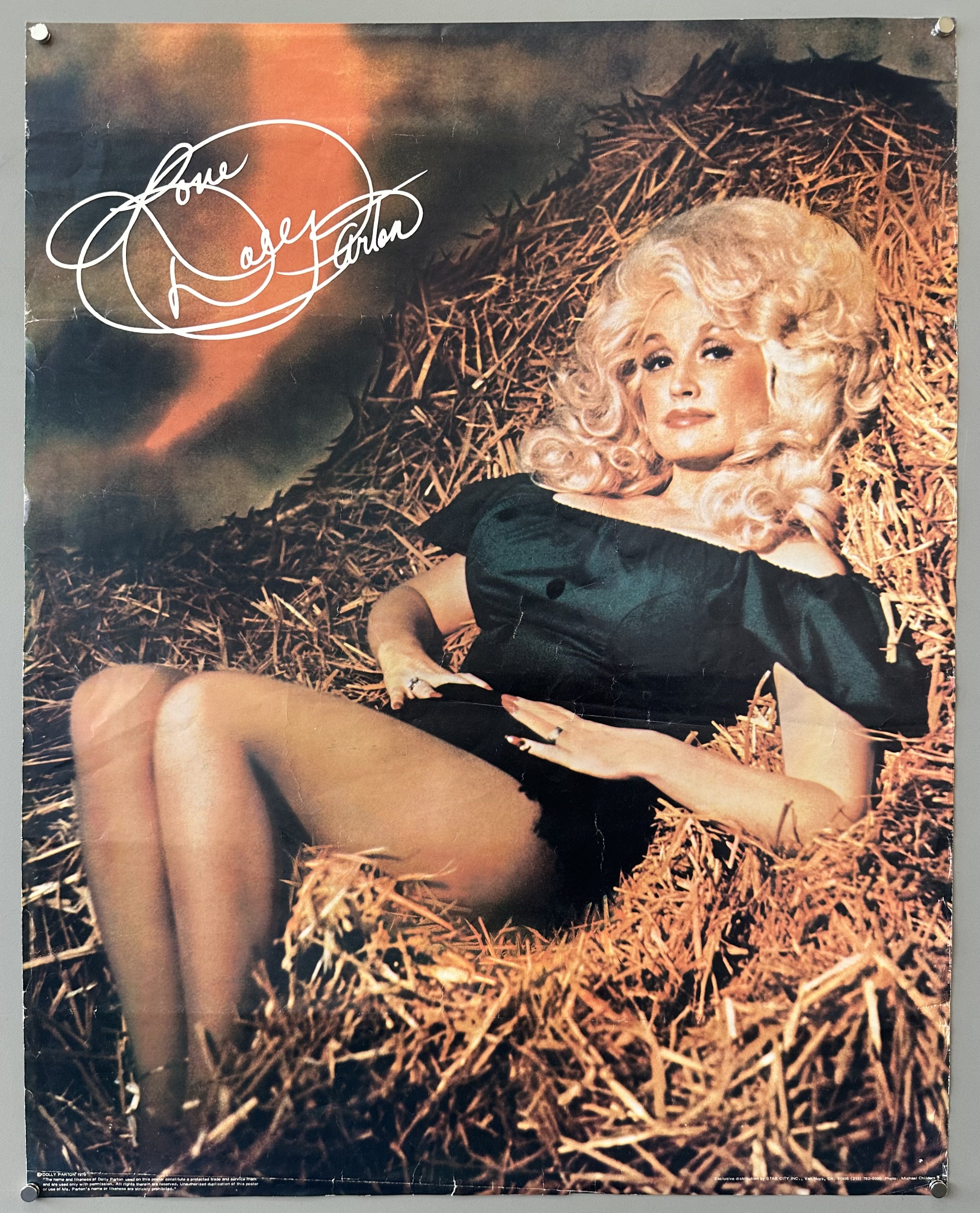 Singer Dolly Parton photographed laying on a bale of hay with cursive white text to the left of her.