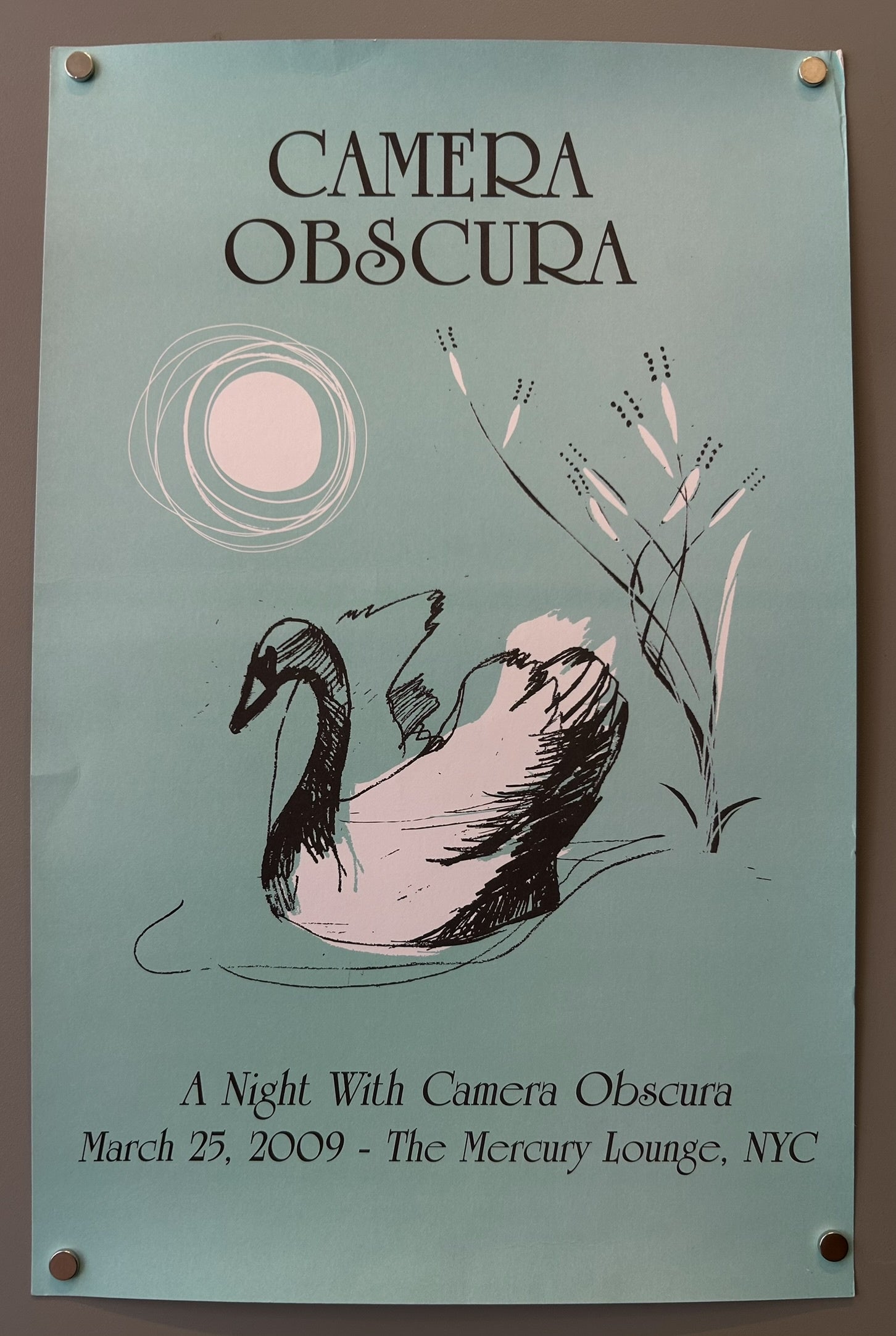 A concert poster for the band Camera Obscura, featuring an illustration of a swan swimming in water under a stylized sun or moon, with tall grasses on the right. Text on the poster reads "CAMERA OBSCURA,"