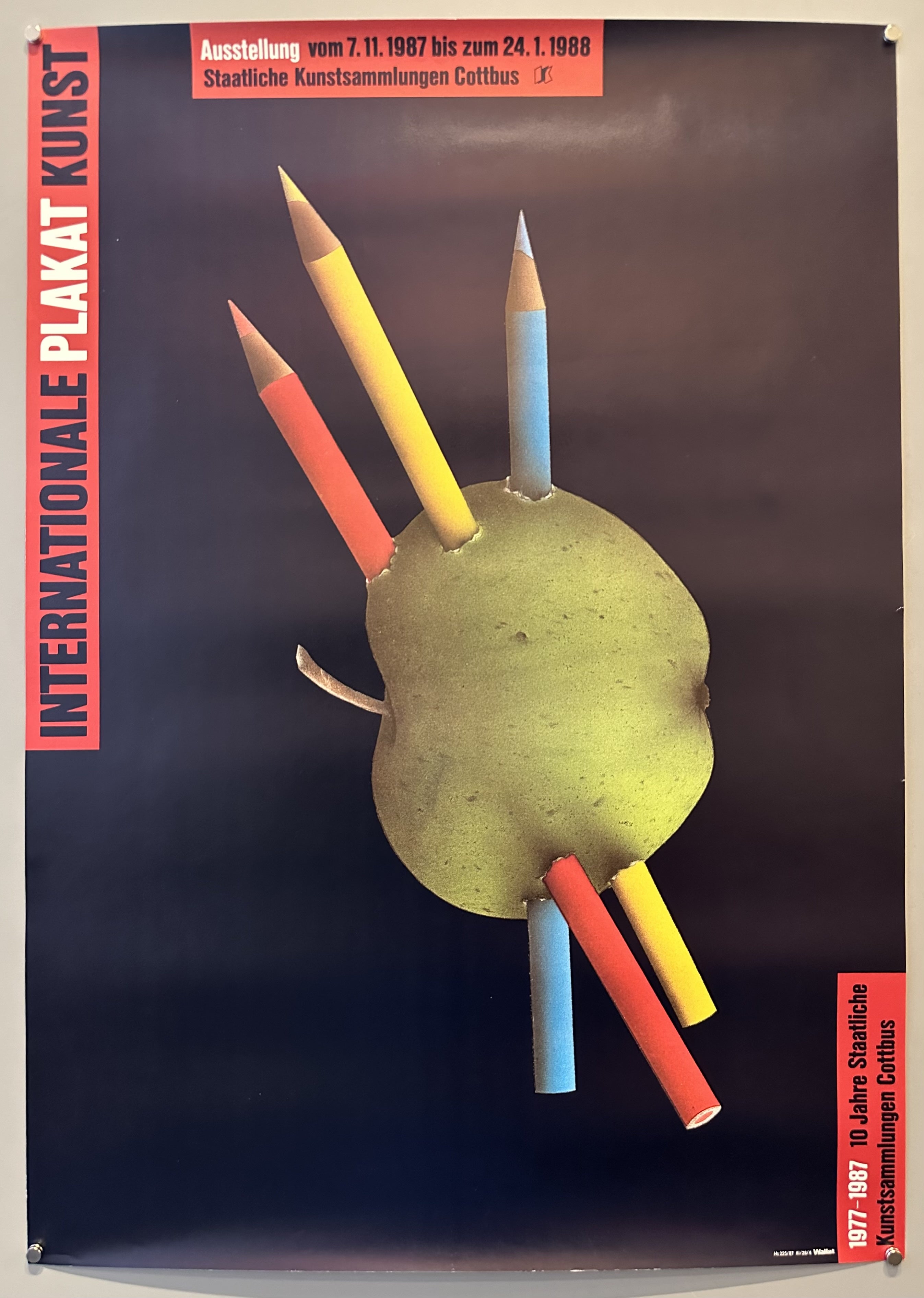 Apple against black background with three colored pencils stuck in it to promote art exhibition in Cottbus, Germany.