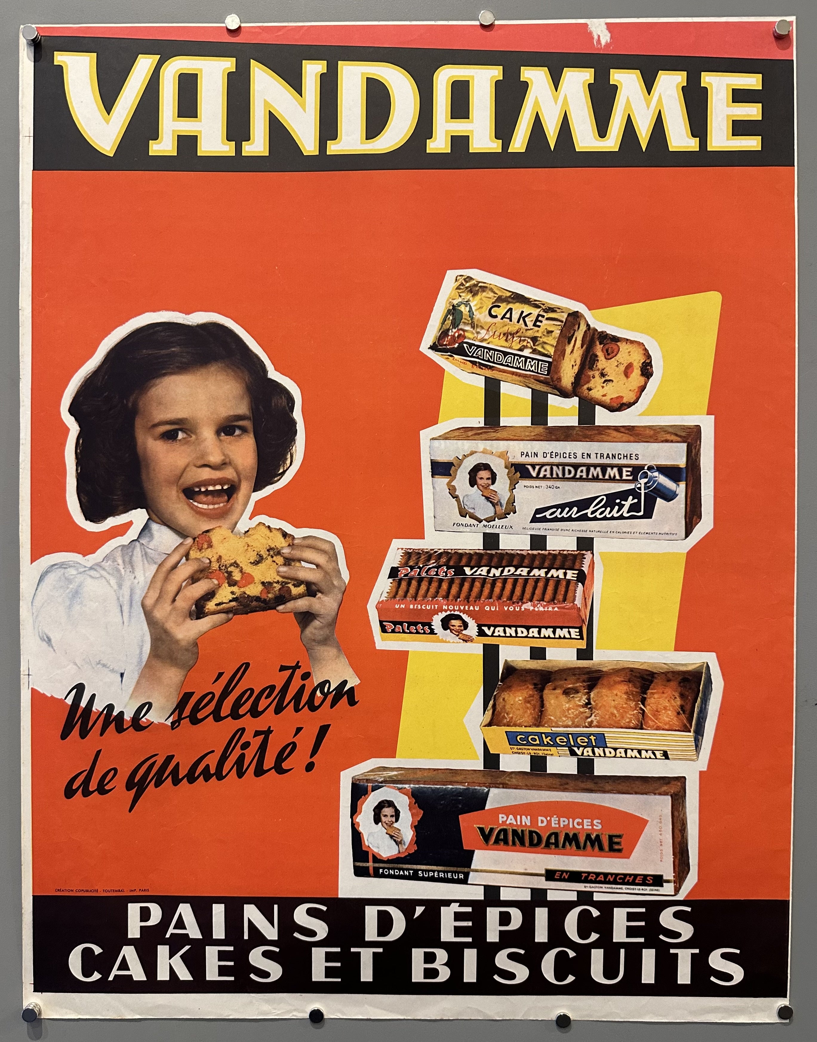 Cut out of child eating a piece of Vandamme fruit cake against red background with other products next to her.
