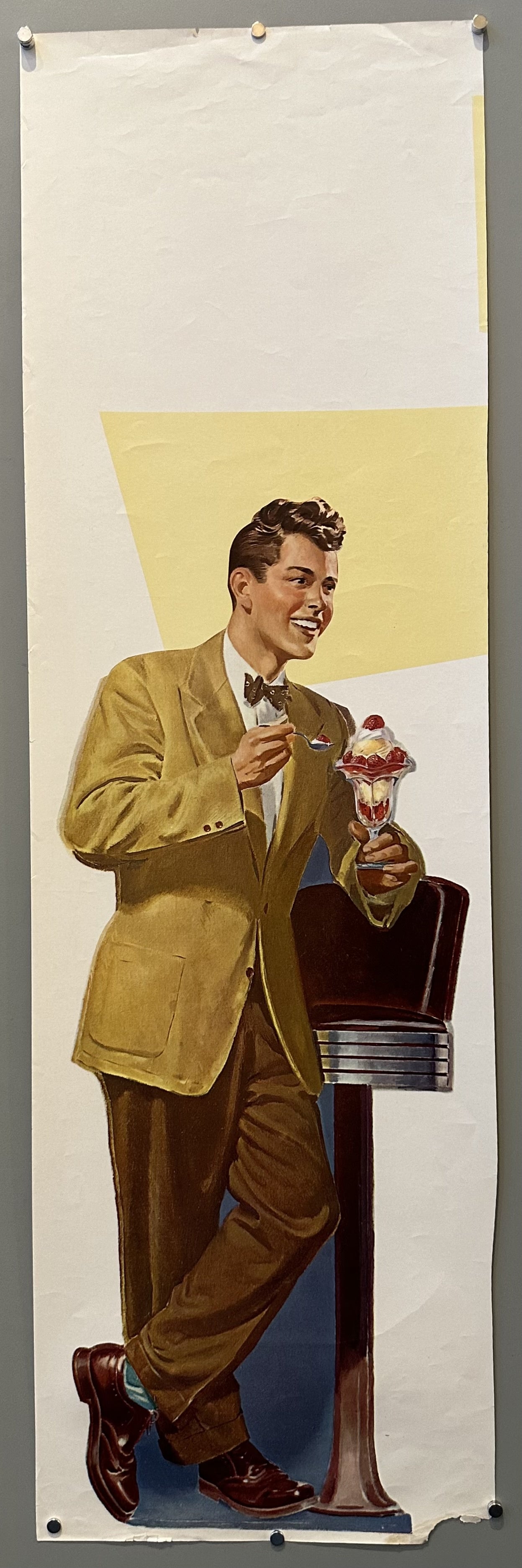 A man leans against a diner bar stool and holds an ice cream sundae.