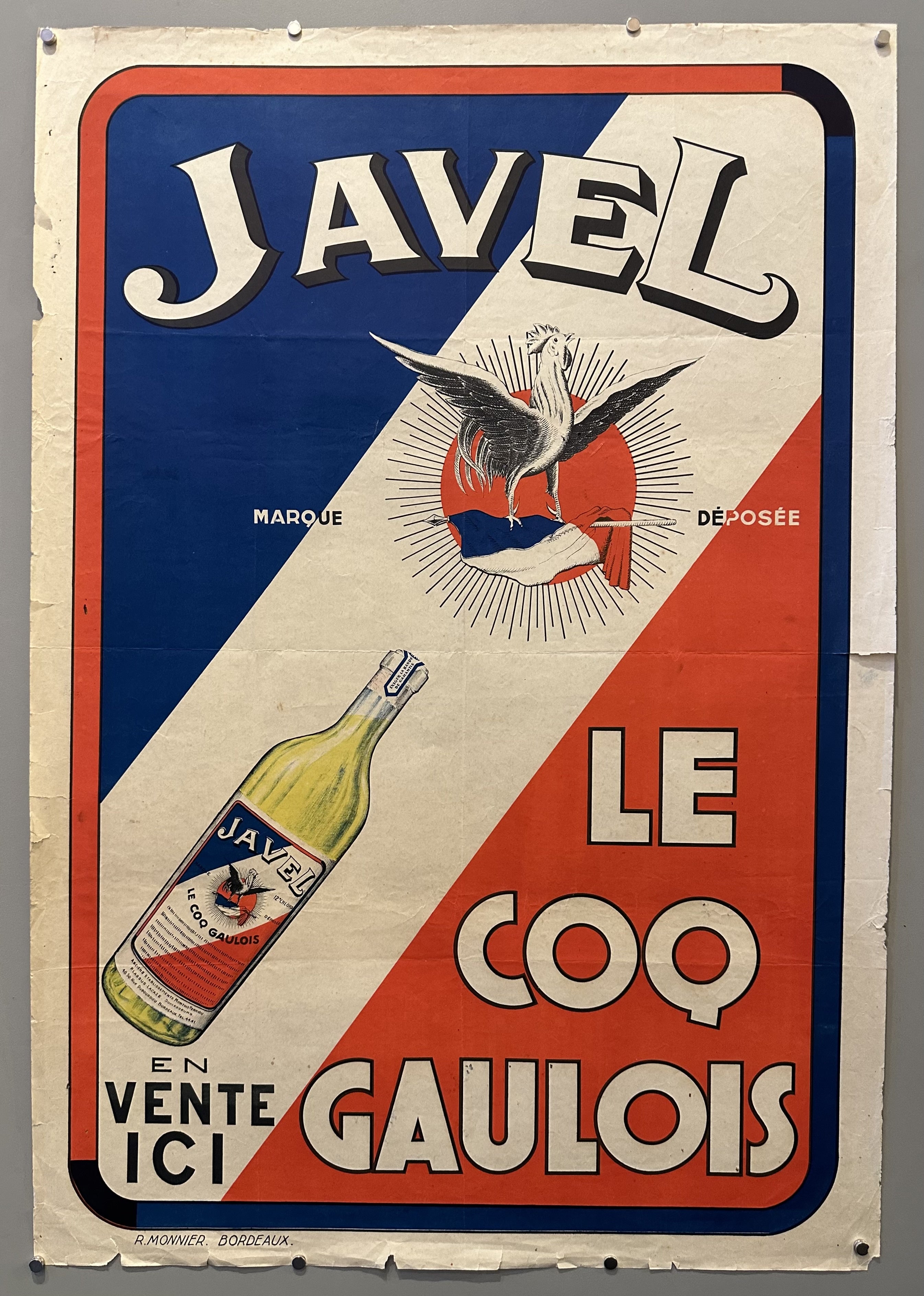 A rooster stands on the French flag with the bottle of bleach under him.