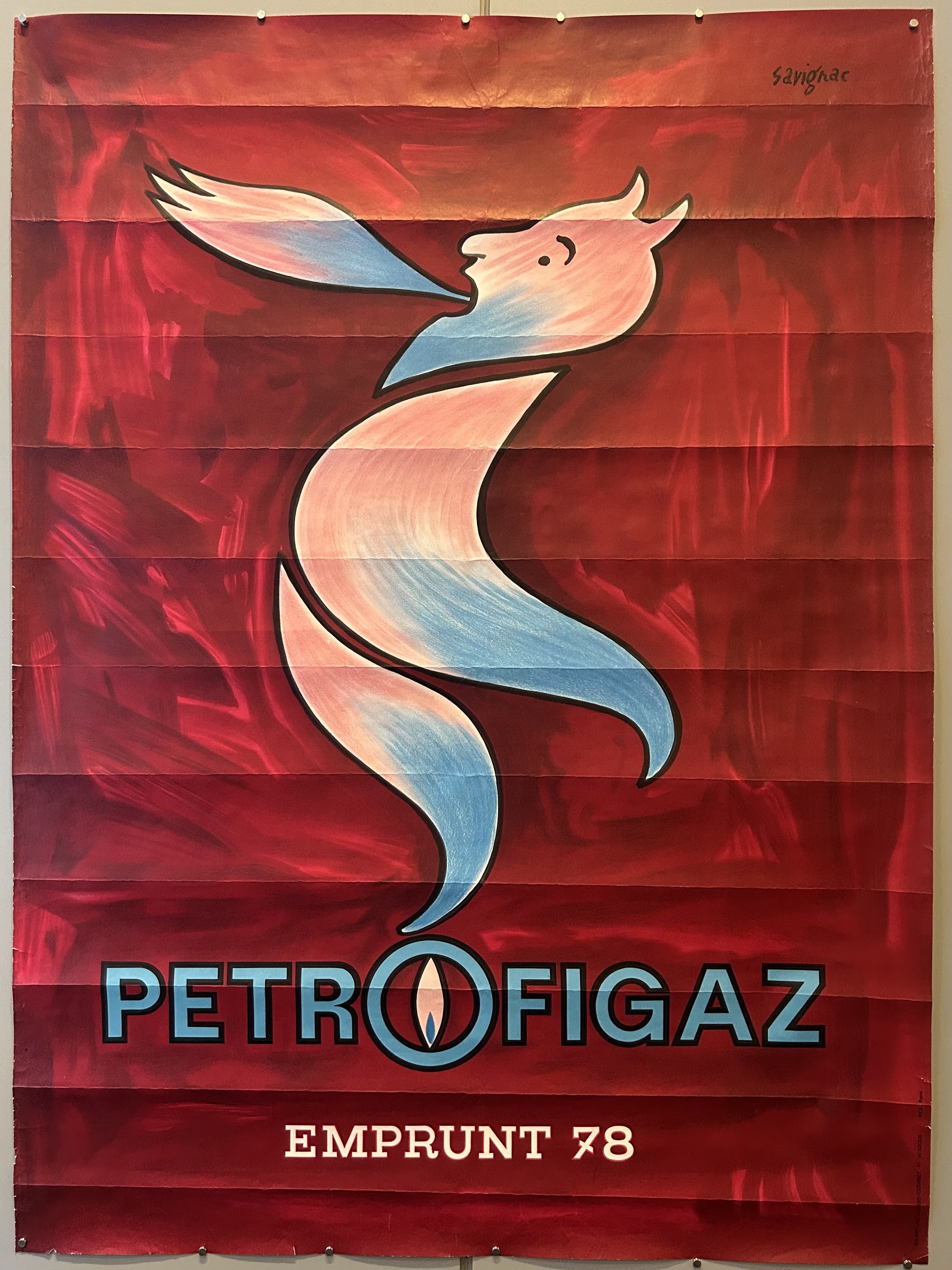 Large poster for gas company with red background and fire-breathing character.