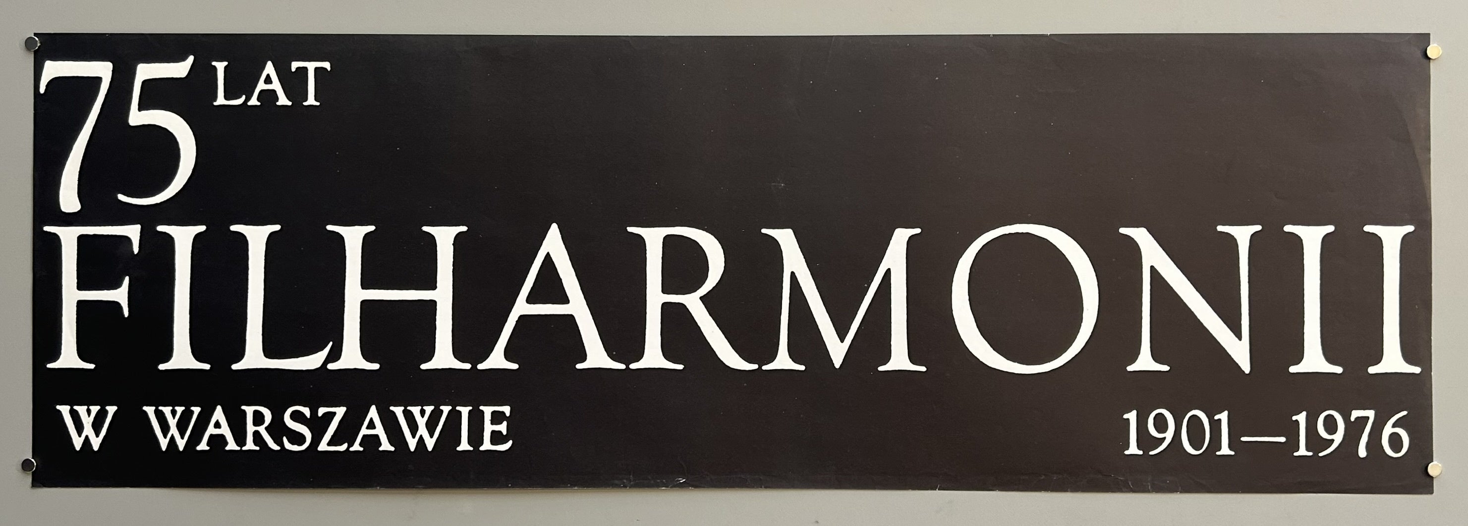 A black banner with white text that reads: "75 LAT FILHARMONII W WARSZAWIE 1901–1976."