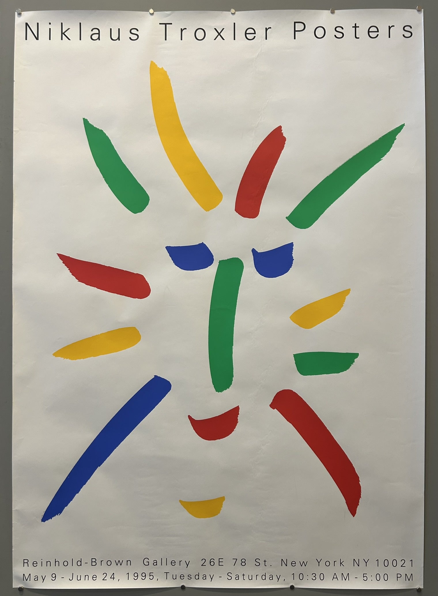 A white poster with colorful, abstract shapes forming a face-like image, predominantly in red, green, blue, and yellow