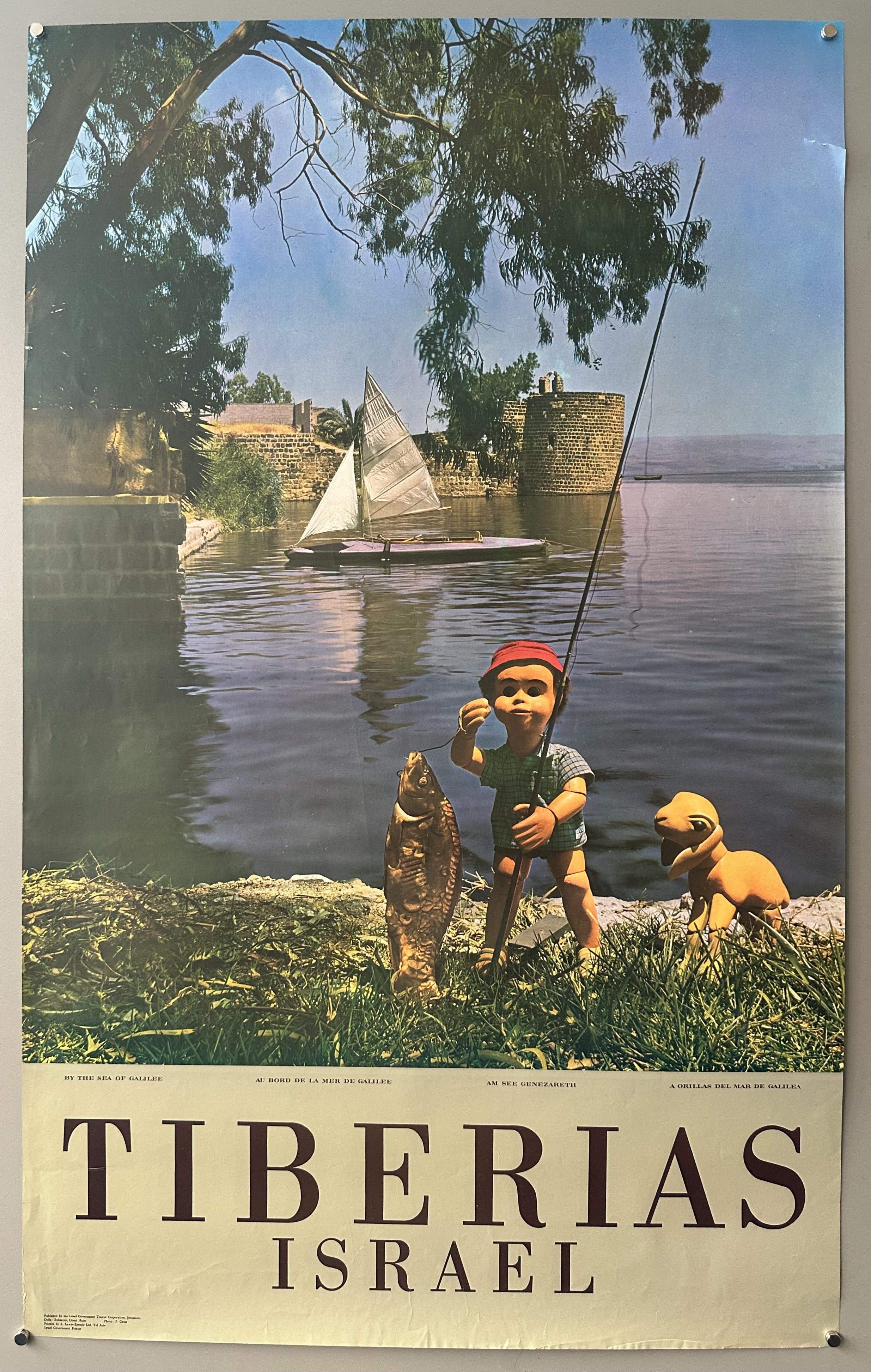 Young boy is featured holding fishinf pole and a large fish he caught, he is standing on the shore of the Sea of Galilee.