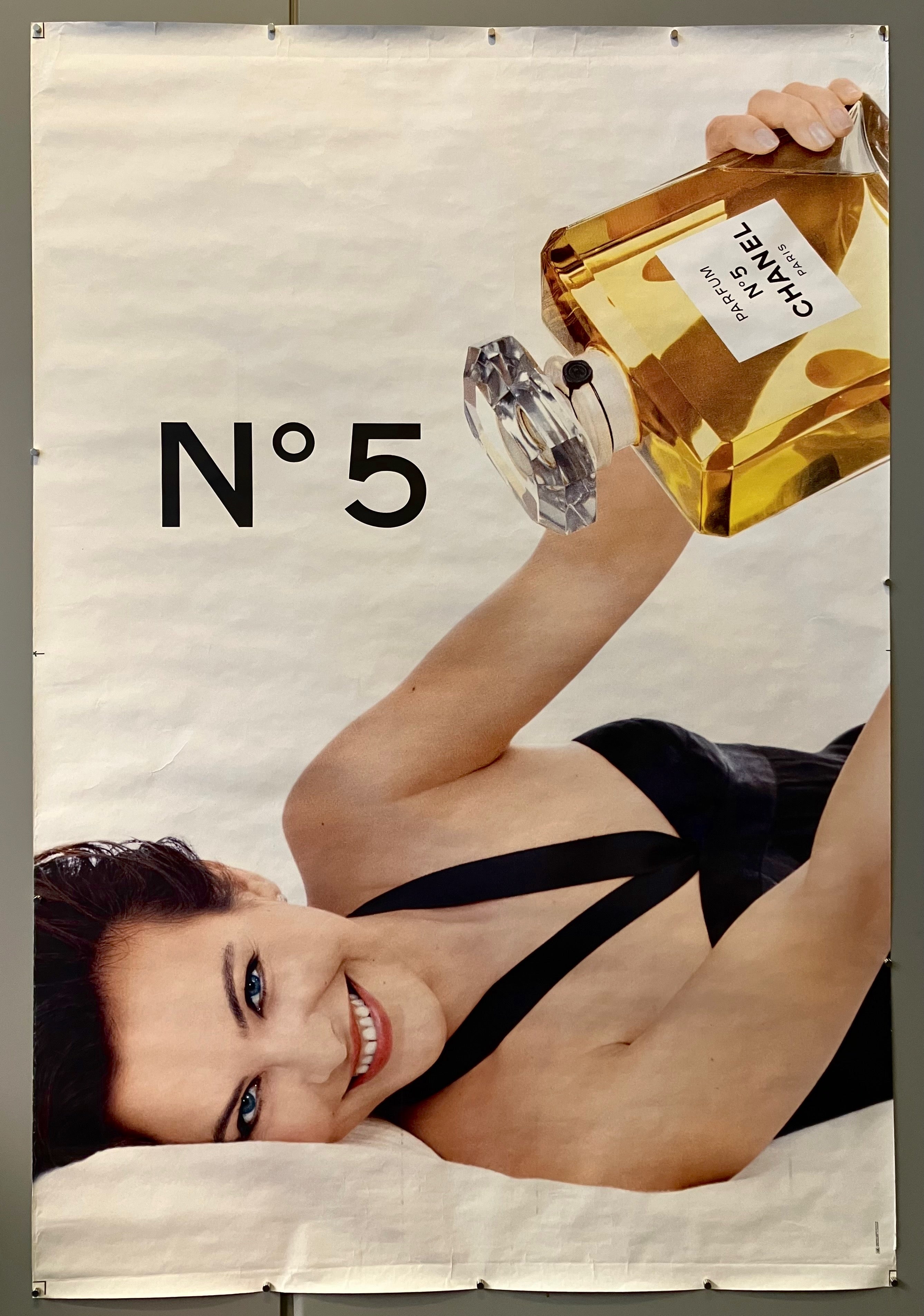 69x47 chanel poster advertising iconic perfume chanel no.5 featuring closeup of actress carole bouquet in black dress holding large bottle of perfume smiling at camera