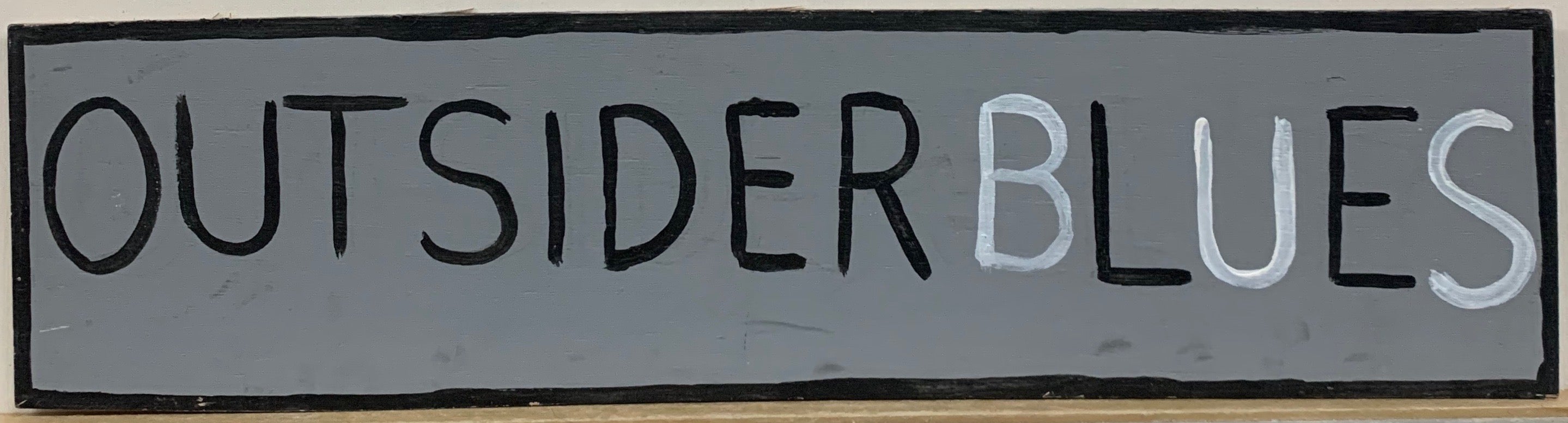 Painting of the phrase "outsider blues," in black lettering except for the "b," "u," and "s" in the world "blues," which are painted white.