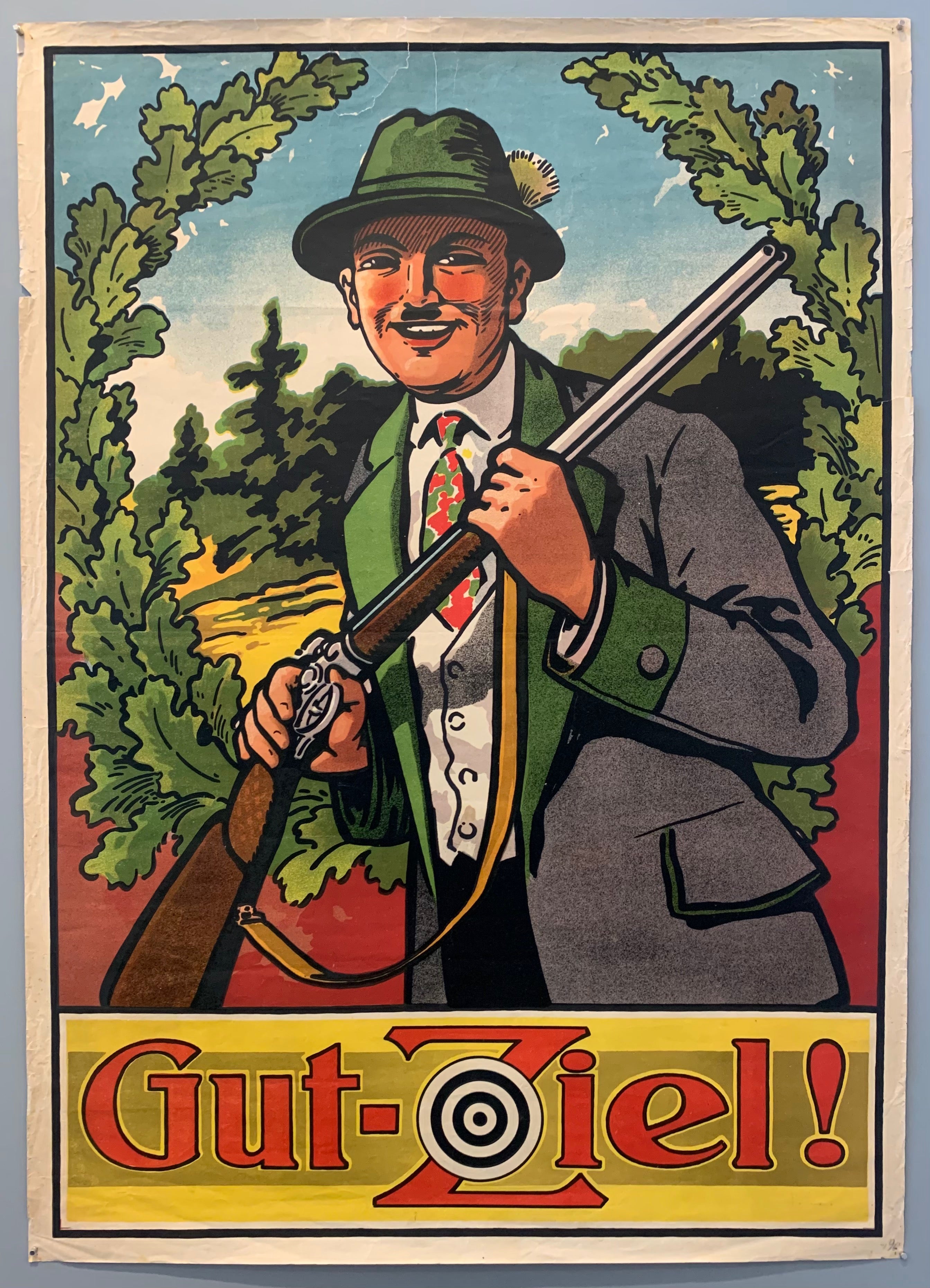 Bavarian hunting poster advertising and encouraging good aim for the contestants of the Schützenfest, in which contestants show off their shooting abilities. This fest is largely celebrated with food, beer and other festivities after the shooting takes place and one person is named the Schützenkönig ("king of marksmen"). The poster welcomes shooters to the 150 year old traditional fest, with a man in Bavarian clothing standing in front of greenery holding his gun with a smile on his face.