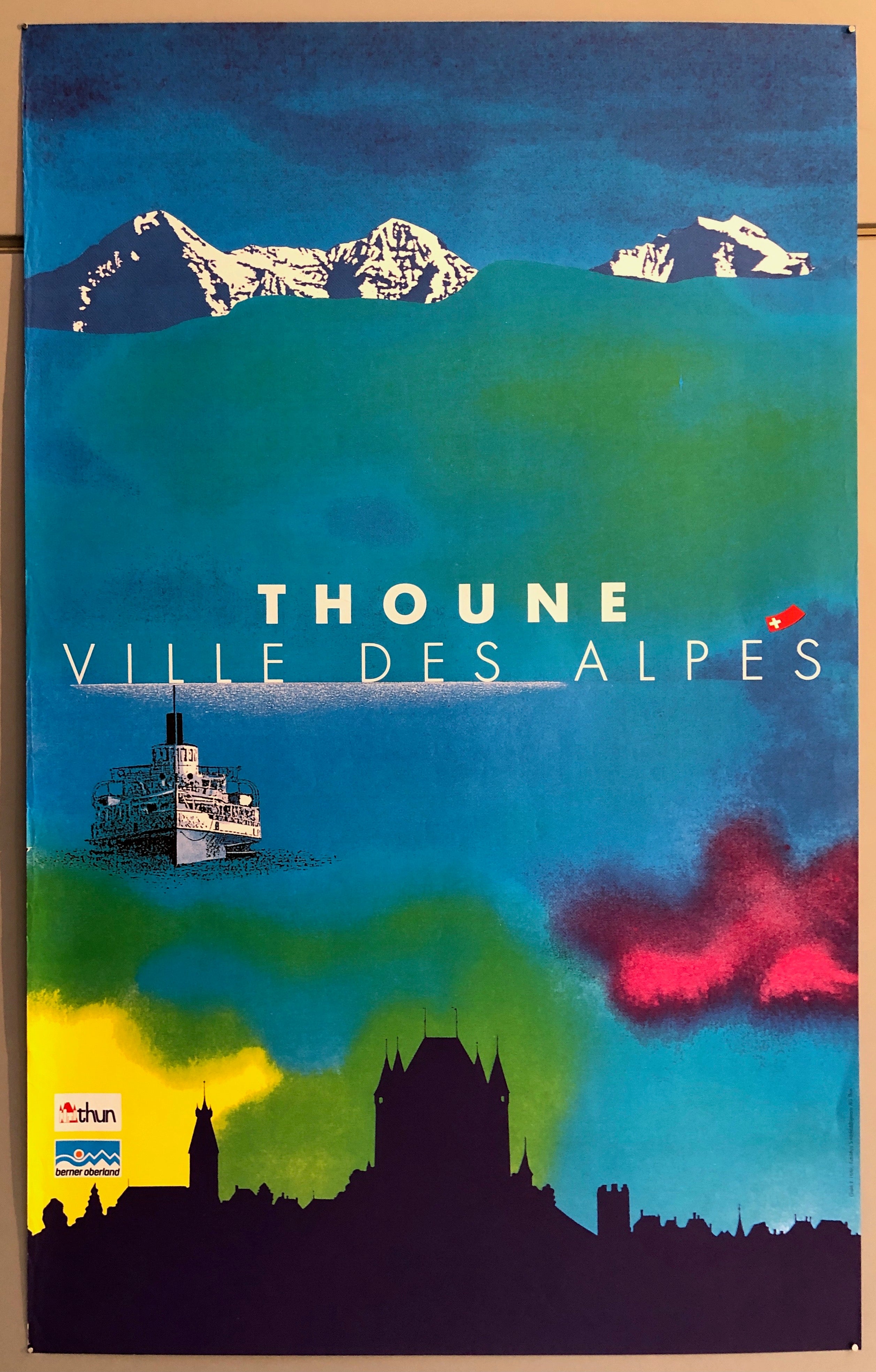 Poster of a colorful sky and water above a silhouette of a Swiss town and below a mountain range.