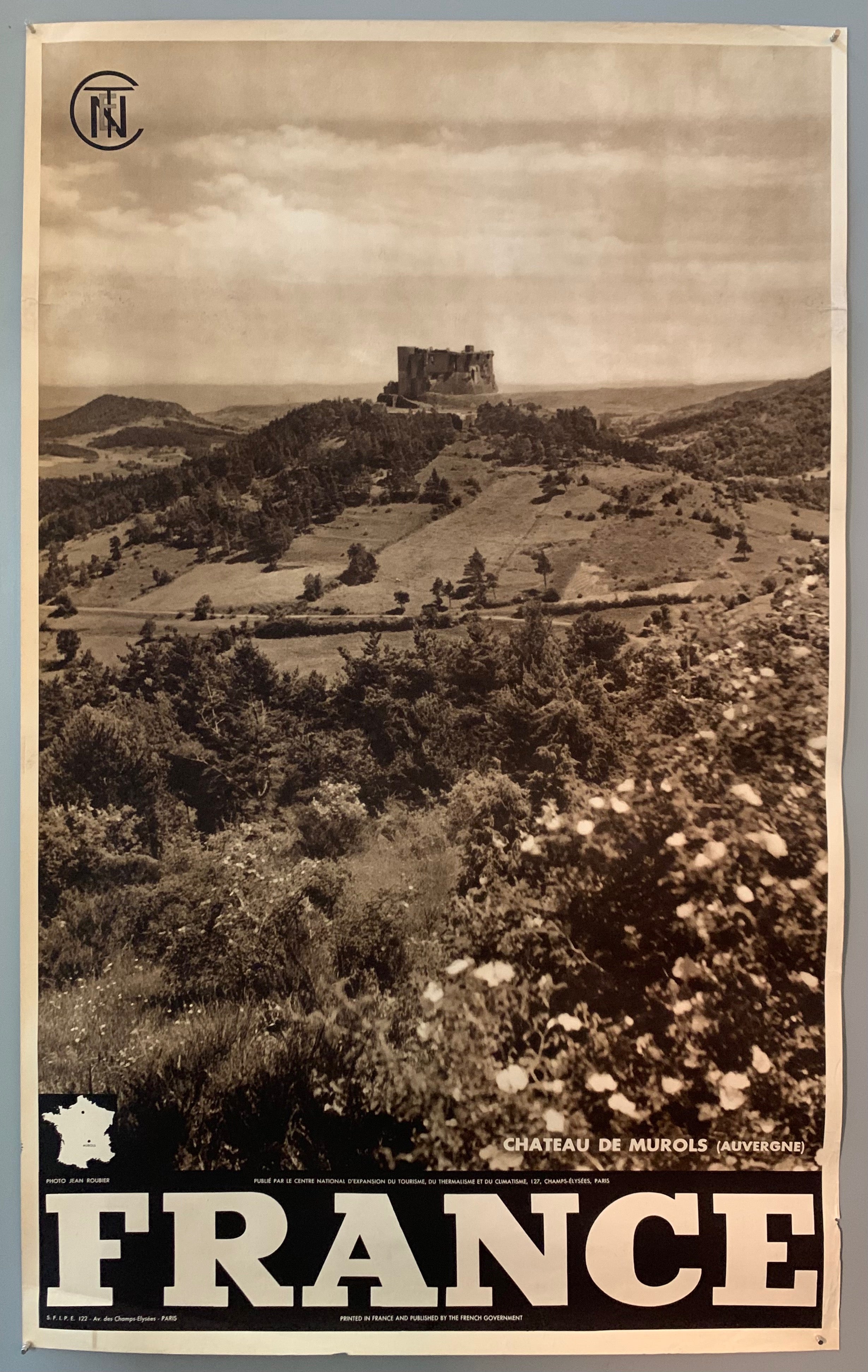 This poster is sepia toned with bold black-and-white writing at the bottom, as well as a tiny map of France. The photograph takes up the majority of the page, with a stamp of the French government at the top left. The photograph mostly contains rolling hills with farmland and trees, and the castle is in the middle, with the sky above it.