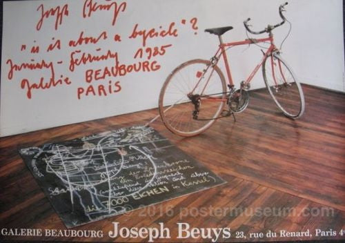 Photograph of a red bicycle attached to a chalkboard lying on the ground with words and abstract lines drawn on it in white chalk. The bicycle and chalkboard are in a white room with a wooden floor. In the top left-hand corner of the photograph are the words "Joseph Beuys "is it about a bycicle" ? January-February 1985 galerie Beaubourg Paris" written in a messy red handwriting. Across the bottom of the poster in a white typeset are the words "Galerie Beaubourg Joseph Beuys 23, rue du Renard, Paris 4eme.